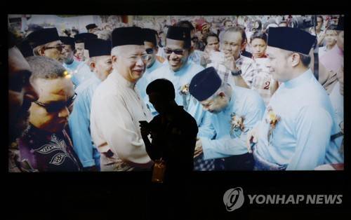 2018년 5월 10일 말레이시아 쿠알라룸푸르 시내에서 여당연합인 국민전선(BN)을 이끄는 나집 라작 총리의 대형 사진 앞에 현지인 남성이 서 있다. [AP=연합뉴스]