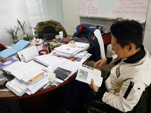 각종 서류와 책으로 가득한 원탁 테이블에서 염 단장이 책을 읽고 있다.