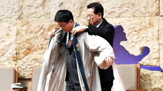 명성교회 김삼환 목사(오른쪽)가 2017년 11월12일 아들 김하나 목사를 담임 목사직에 임명하는 취임식에서 김하나 목사에게 직접 착용했던 성의를 입혀주고 있다.  국민일보DB