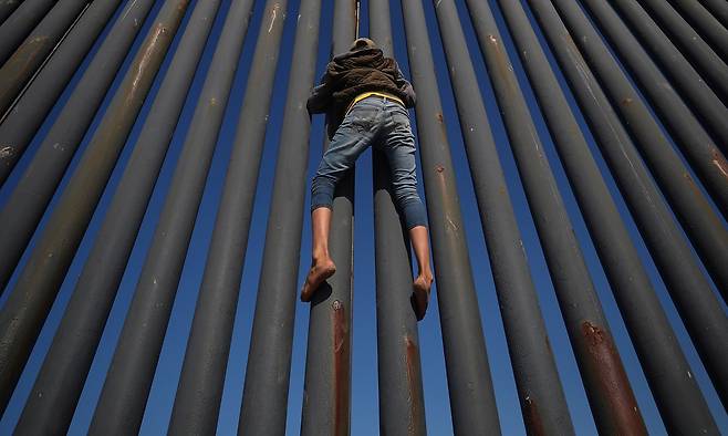 한 이민자가 18일(현지시간) 멕시코 북부 티후아나의 미국-멕시코 국경 담장을 오르고 있다. [로이터=연합뉴스]