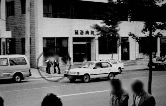 1987년 당시 병원을 나서던 피해자(점선내 앞사람)가 복지원 운전기사(뒷사람)와 함께 복지원 소유 봉고차에 타기위해 걸어가고 있다. 당시 경찰관은 건물옆에서 주머니에 손을 넣은채 엉뚱한 방향을 바라보고있었다. [중앙포토]