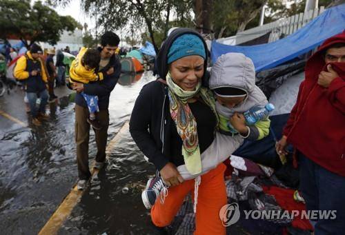 멕시코 티후아나 머물고 있는 중미 이주자(캐러밴)들이 29일(현지시간) 갑자기 내린 폭우에 아이들을 데리고 급히 다른 곳으로 이동하고 있다. [AP=연합뉴스]