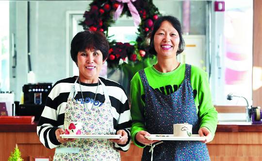 장승포항이 내려다보이는 애광원 내 카페 윈드밀 테라스에서 근무하는 지적장애인 이옥녀(왼쪽)씨와 주은미씨가 직접 만든 커피를 들고 웃고 있다.