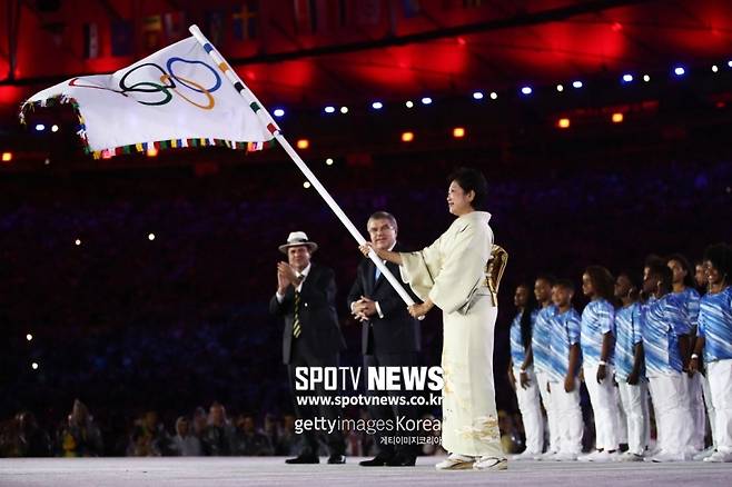 ▲ 2016년 리우데자네이루올림픽 폐막식에서 차기 개최지인 도쿄의 고이케 유리코 도쿄도지사(가장 오른쪽)가 토마스 바흐 IOC 위원장(가운데)에게서 올림픽기를 받고 있다.