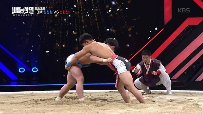 <한국방송>(KBS) 스포츠예능 <씨름의 희열>에 출연하는 두 선수가 모래판 위에서 서로 샅바를 잡고 힘을 겨루고 있다. 다양한 각도에서 찍은 슬로모션 화면들이 씨름의 묘미를 제대로 전달해준다. 방송화면 갈무리
