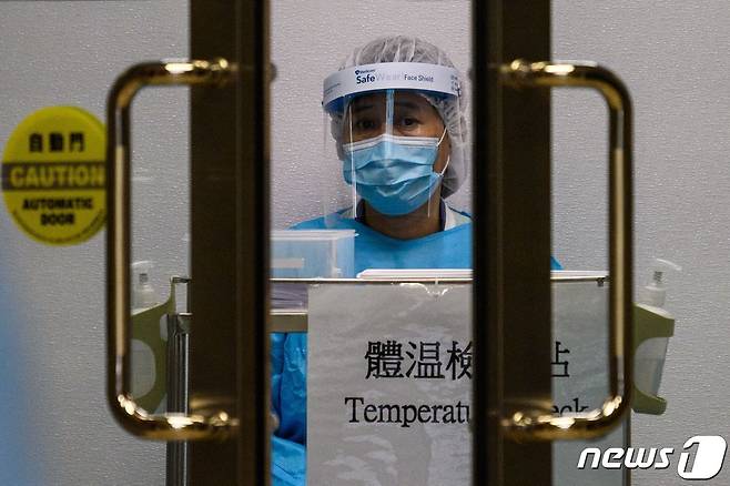 보호복을 입은 병원 관계자가 프린세스마가렛병원으로 들어오는 사람들의 체온을 제고 있다. 이 병원에서는 4일 신종 코로나바이러스 감염증 치료를 받던 39세 남성이 사망했다. © AFP=뉴스1
