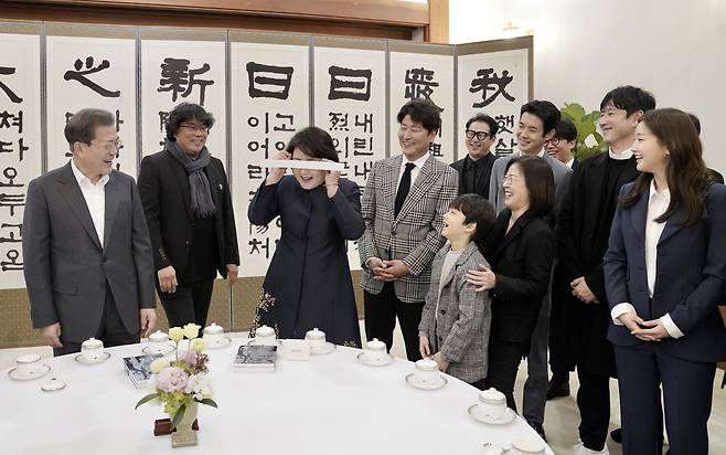 김정숙 여사(왼쪽 셋째)가 20일 청와대에서 영화 ‘기생충’ 포스터에 나와 화제를 모은 ‘눈가리개’를 제작진으로부터 선물 받아 착용해 보고 있다. 청와대사진기자단