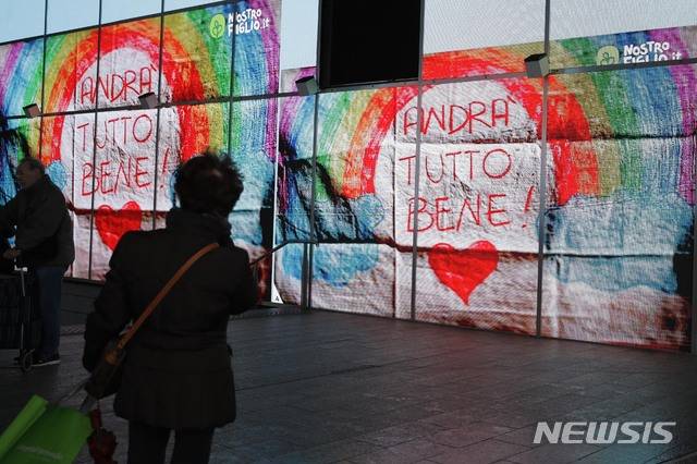 [밀라노=AP/뉴시스]14일(현지시간) 이탈리아 밀라노 거리에서 한 여성이 전광판에 나오는 "다 잘 될 거야"(Andra tutto bene)라고 쓰인 무지개 그림을 바라보고 있다. 이탈리아 정부가 신종 코로나바이러스 감염증의 확산을 줄이기 위해 전국을 봉쇄한 가운데 어린이들이 그린 무지개 그림이 소셜 미디어뿐만 아니라 주요 도시의 발코니나 창문, 전광판 등에 등장해 서로를 응원하고 있다. 2020.03.15.