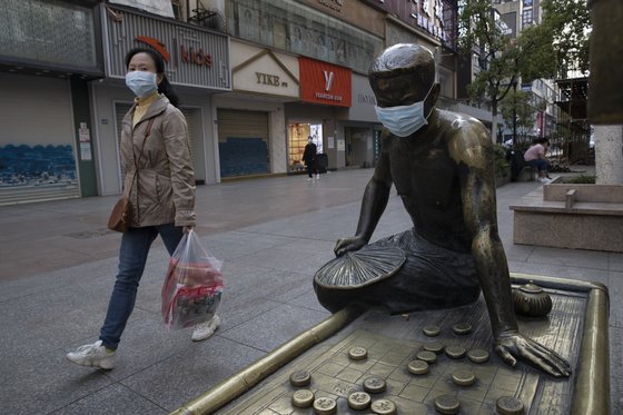 지난달 13일 중국 후베이성 우한에서 한 시민이 마스크를 쓴 채 마스크를 쓴 동상 옆을 지나가고 있다.[AP=연합뉴스]