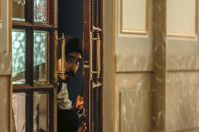 테러범들이 인질극을 벌인 타지마할 호텔의 직원 아르준(데브 파텔 분)이 투숙객들을 대피시키기 위해 테러범들의 동태를 살피는 모습. 실제로 당시 타지마할 호텔에는 희생적으로 투숙객들을 구해낸 용감한 직원들이 있었다. [에스와이코마드 제공]