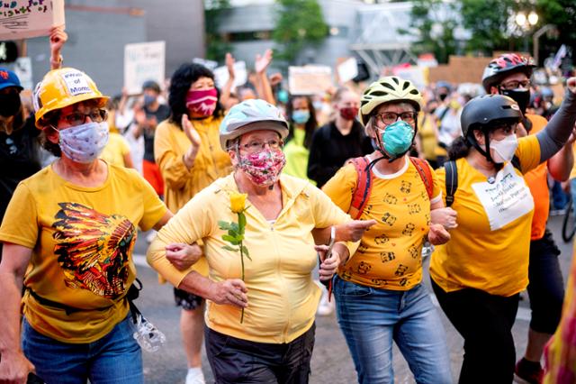 미국 오리건주 포틀랜드에서 20일 '흑인의 생명도 소중하다(Black Lives Matt)' 시위 중 연방요원들로부터 시위대를 보호하기 위해 나선 노란색 셔츠를 입은 여성들이 팔짱을 끼고 서서 '엄마들의 벽'을 만들고 있다. 포틀랜드=AP 연합뉴스