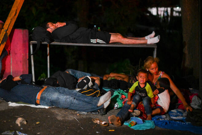 1일(현지시간) 온두라스 국경을 넘은 이민자들이 과테말라 엔트 레 리오스에서 쪽잠을 자며 쉬고 있다. 엄마의 무릎에 앉은 한 아이가 울음을 터뜨리고 있다. (Photo by Johan ORDONEZ / AFP)