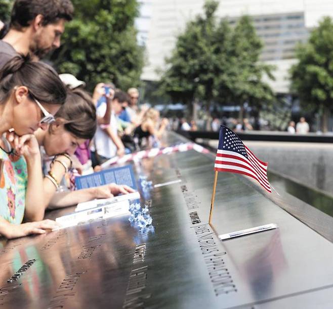 9·11 추모 기념 공원을 찾은 추모객들이 청동 패널에 적힌 희생자들 이름을 읽고 있다. 외롭게 꽂힌 성조기가 이채롭다.
