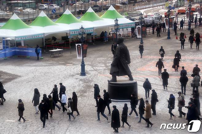 전날부터 내린 눈으로 도심 곳곳에 빙판길이 생긴 18일 오전 서울 중구 서울역광장에 마련된 코로나19 임시 선별진료소에서 검사를 받기 위해 줄 선 인파와 출근하는 시민들로 북적이고 있다. 2020.12.18/뉴스1 © News1 이동해 기자