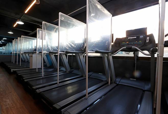 7일 오후 정부 방역조치의 형평성을 주장하며 매장의 조명을 켜놓는 ‘오픈 시위’가 진행 중인 서울 마포구 태영휘트니스 러닝머신에 코로나19 확산 방지를 위한 가림막이 설치되어 있다. 이날 정부는 모든 실내체육시설에 대해 이용대상을 아동·청소년으로, 운영 목적도 교습으로 한정해 동시간대 9인 이하 운영을 허용했다. 연합뉴스