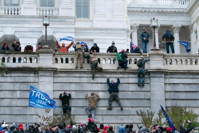 도널드 트럼프 대통령의 지지자들이 6일 워싱턴의 미 국회의사당 서쪽 벽을 오르고 있다. AP 연합뉴스