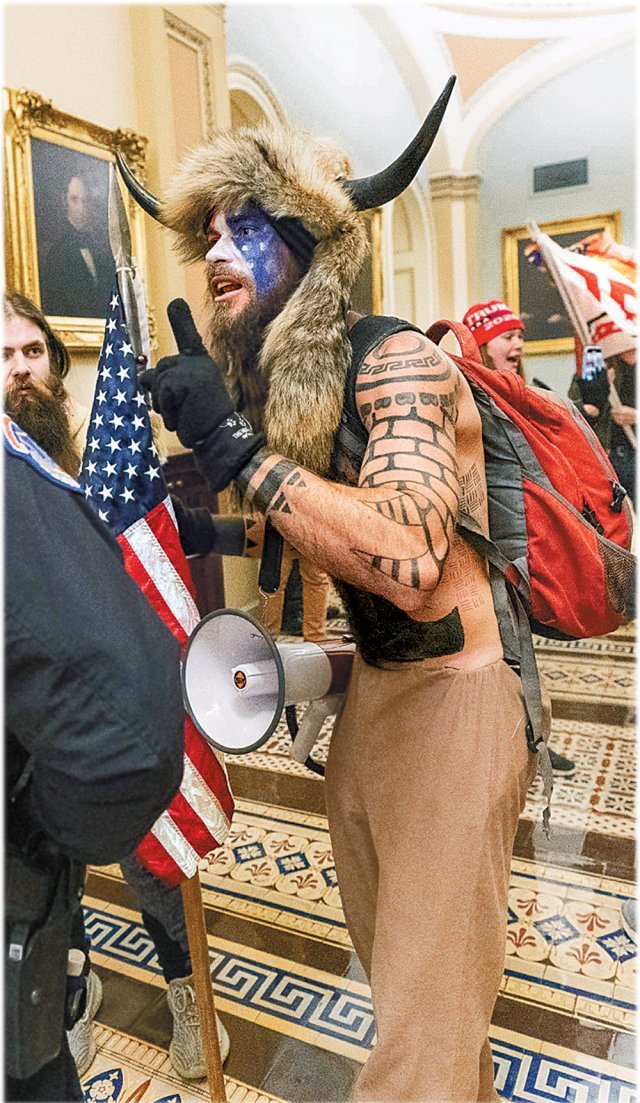 6일(현지 시간) 미국 워싱턴 의회에 난입한 미 극우단체 ‘큐어논’ 회원 제이크 앤절리(32)가 얼굴에 성조기 문양을 하고 뿔 달린 모자를 쓴 채 경찰과 대치하고 있다. 워싱턴=AP 뉴시스