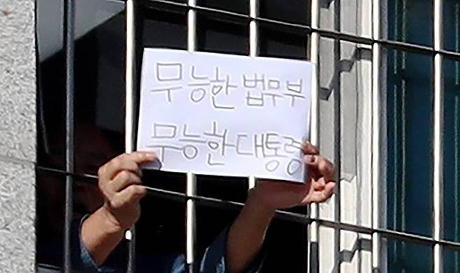 지난 6일 서울동부구치소에서 한 수용자가 ‘무능한 법무부 무능한 대통령’이라고 쓴 종이를 창문 밖 취재진에게 내보이고 있다. 연합뉴스
