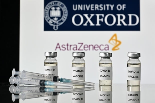 옥스퍼드대와 아스트라제네카의 로고를 배경으로 코로나19 백신 스티커가 부착된 병과 주사기가 놓여있는 모습/사진=연합뉴스