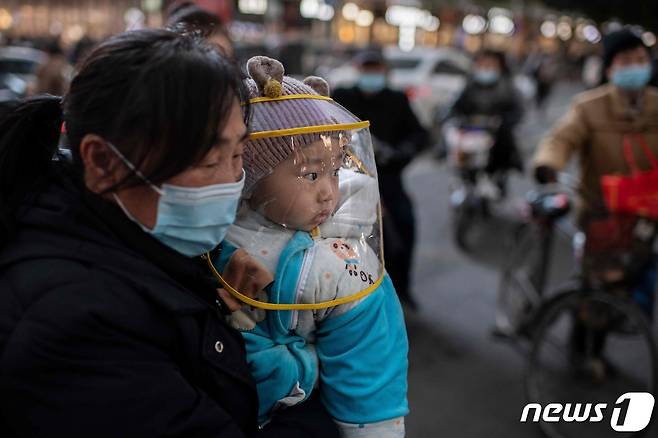 지난 13일 중국 후베이성 우한시의 쇼핑몰 앞에서 마스크를 쓴 한 여성이 아기를 안고 있다. © AFP=뉴스1