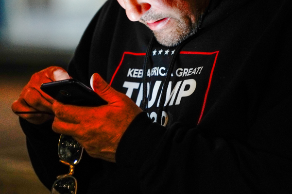 지난해 11월5일(현지 시각) 미 위스콘신주 최대 도시인 밀워키 외곽에서 열린 도널드 트럼프 지지자들의 대선 불복 시위에서 '트럼프 2020' 로고가 적힌 옷을 입은 한 남성이 휴대전화를 사용하고 있다./로이터연합뉴스