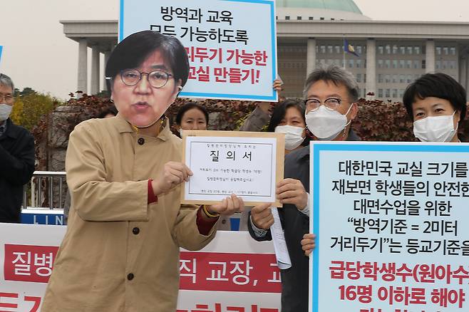 현직 교장 및 교사들이 지난해 10월21일 오후 국회 정문 앞에서 ‘사회적 거리두기 2m - 학급당 학생 수 16명을 촉구한다’ 기자회견을 하고 있는 모습. 이들은 “사회적 거리두기 2m를 유지하면서 등교 수업을 하려면, 3분의1 등교나 3분의2 등교라는 기준이 아니라, 학급당 학생수 16명 이하이어야 한다”며 정은경 질병관리청장에게 질의하는 퍼포먼스를 했다. [연합]