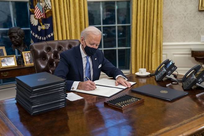 조 바이든 미국 대통령이 20일(현지 시간) 취임식 직후 백악관 집무실에서 각종 행정명령에 서명하고 있다. 바이든 대통령은 서명하는 중에도 얼굴에 마스크를 착용했다. 연합뉴스 제공