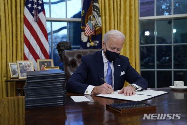 [워싱턴=AP/뉴시스]조 바이든 미국 대통령이 20일(현지시간) 백악관 집무실에서 첫 행정명령에 서명하고 있다. 2021.01.21.