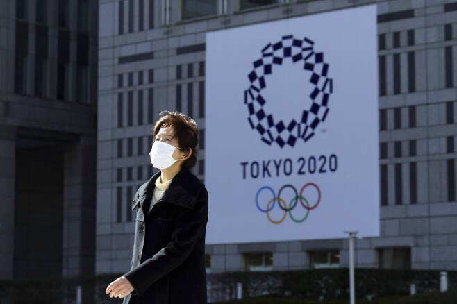 지난 19일 일본 도쿄에서 한 여성이 올림픽 배너가 걸려있는 건물 앞올 마스크를 낀 채 지나가고 있다. AP연합뉴스