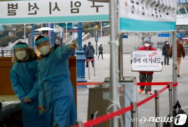 (서울=뉴스1) 안은나 기자 = 21일 오전 서울역 광장에 마련된 중구 임시선별검사소에서 한 시민이 '코로나19 함께 이겨내요 화이팅'이라 써진 손팻말을 들고 있다. 이날 0시 기준 신종 코로나바이러스 감염증(코로나19) 신규 확진자는 지역 발생 380명, 해외유입 21명으로 총 401명 발생했다. 2021.1.21/뉴스1  <저작권자 ⓒ 뉴스1코리아, 무단전재 및 재배포 금지>
