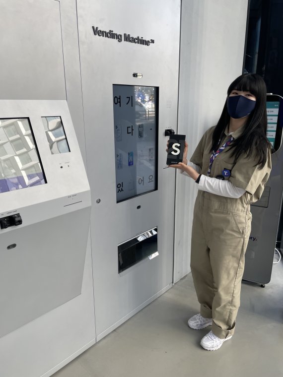 SK텔레콤 직원이 홍대 플래그십 매장 'T팩토리'에 설치된 무인 자판기에서 뽑은 휴대폰을 들어보이고 있다. SKT 제공