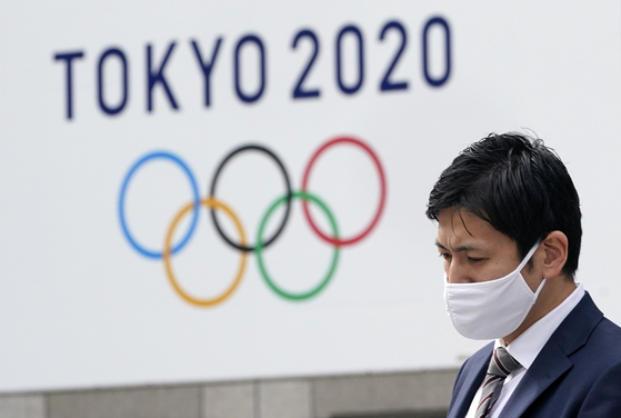 A citizen wearing a face mask passes by a Tokyo Olympics sign board near the Tokyo city hall recently. [EPA/YONHAP]