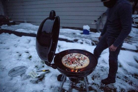 미국을 덮친 이상 한파와 폭설로 정전과 단수 사태를 겪은 텍사스 샌마커스에서 한 남자가 바베큐 틀에 불을 지펴 냉동 피자를 녹이고 있다. 로이터=연합뉴스