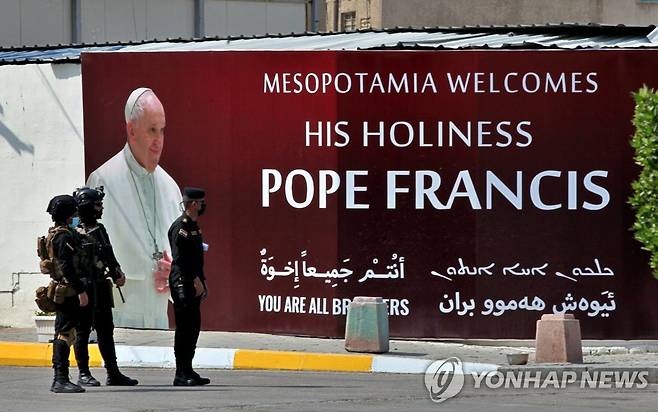 프란치스코 교황이 이라크 땅에 첫발을 내딛는 5일(현지시간) 교황 환영 포스터가 걸린 벽 앞에서 무장 보안요원들이 경비를 하는 모습. [AP=연합뉴스]