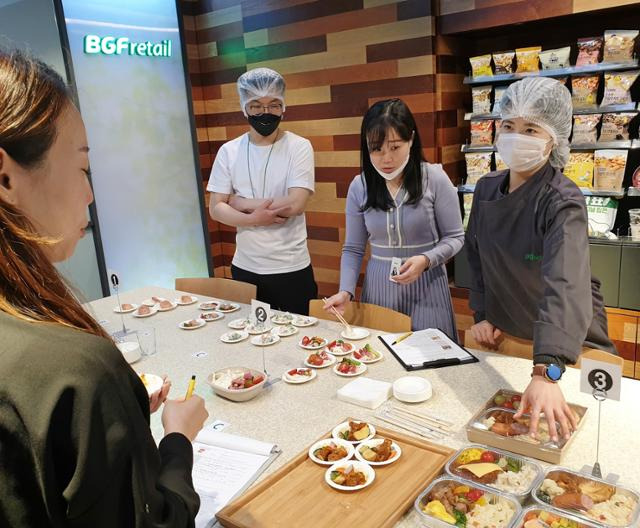 편의점 CU를 운영하는 BGF리테일 상품개발팀 직원들이 품평회를 하고 있다. 사진은 코로나19 방역지침이 강화되기 전인 지난해 가을 대면 품평회에서 김소희(맨 오른쪽) 상품개발자(MD)가 '신상출시 편스토랑' 촬영 중 연예인이 만든 음식에 대해 설명하는 모습. 방역을 위해 최근엔 품평용 상품을 퀵서비스로 받아 시식하고 있다. BGF리테일 제공