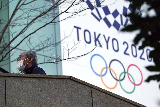 마스크를 쓴 한 남성이 지난 2월 25일 도쿄 올림픽 현수막 앞을 걷고 있다. AP=연합뉴스