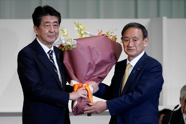 아베 신조(왼쪽) 전 일본 총리가 지난해 9월 14일 자민당 총재 선거에서 스가 요시히데 당시 관방장관이 당선되자 꽃다발을 주고 있다. 도쿄=AP 연합뉴스