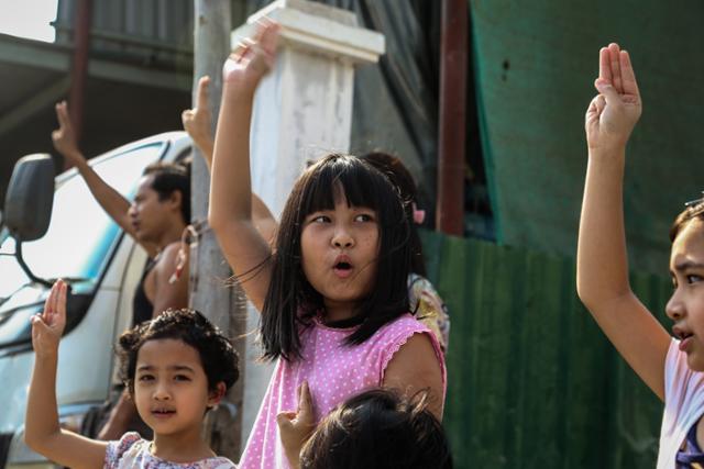 11일(현지시간) 미얀마 제2의 도시 만달레이 거리를 행진하는 민주화 시위대를 향해서 어린이들이 연대의 의미로 세 손가락을 들어보이고 있다. 미얀마의 인권단체인 정치범지원연합(AAPP)에 따르면 2월 1일 미얀마 군부가 쿠데타를 일으킨 이후 적어도 700명 이상이 목숨을 잃었다. 만달레이=EPA 연합뉴스