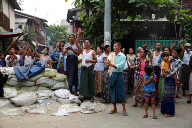 미얀마 만달레이 주민들이 군경의 기습 수색을 막기 위해 마을 입구에 모래주머니를 쌓아 놓았다. 뒤편으로 위성TV 접시 안테나가 보인다. 시민들이 지나가는 시위대에게 세 손가락 경례를 하고 있다. 만달레이=AFP 연합뉴스