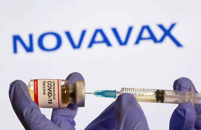 A woman holds a small bottle labeled with a "Coronavirus COVID-19 Vaccine" sticker and a medical syringe in front of displayed Novavax logo in this illustration taken, October 30, 2020. (Reuters-Yonhap)
