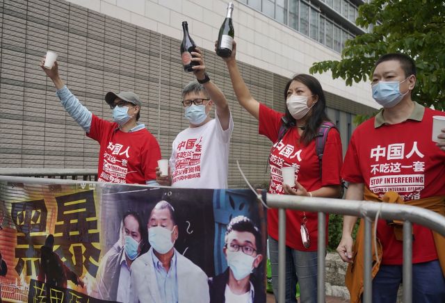 홍콩 친중 시위대가 지난 16일 반중 매체인 빈과일보의 사주 지미 라이를 포함한 범민주진영 인사들의 재판이 열린 법원 주변에서 실형 선고에 기뻐하며 샴페인 병을 치켜들고 있다. AP연합뉴스