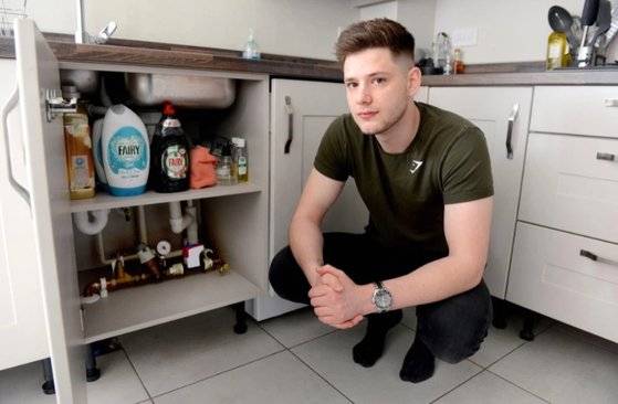 영국 청년 애슐리 더글라스가 배관 수리를 받은 자신의 집 싱크대 옆에 앉아 있다. [트위터 캡처]