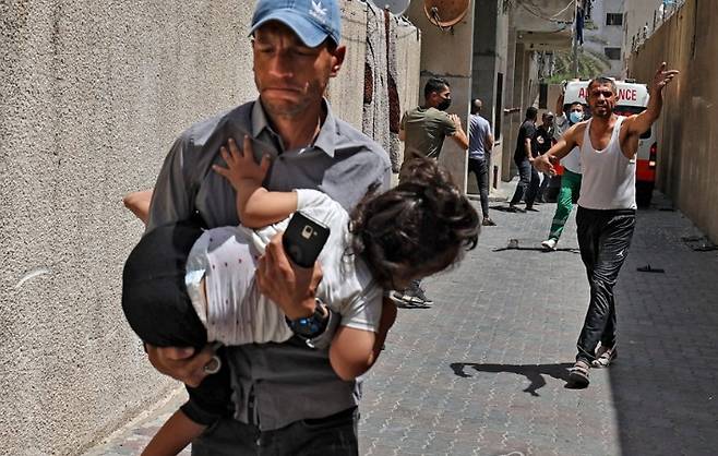 지난 11일(현지시간) 팔레스타인 가자지구의 중심도시 가자시티에서 이스라엘군의 공습으로 한 남성이 아이를 품에 안은 채 대피하고 있다. 연합뉴스
