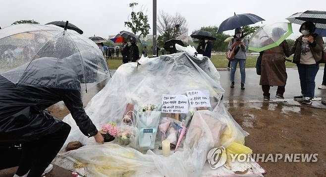 수북이 쌓인 추모 꽃다발 지난 16일 오후 서울 반포한강공원 수상택시 승강장 인근에서 열린 '고 손정민 군을 위한 평화집회'에서 한 참가자가 손 씨를 위한 추모 공간에 꽃다발을 놓고 있다. [연합뉴스 자료사진]