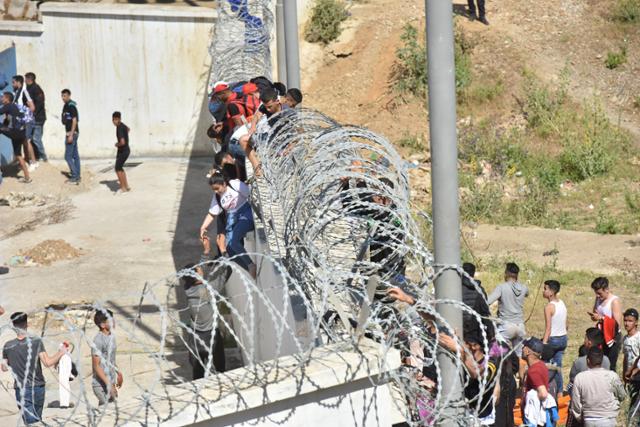 18일 아프리카 출신 이주민들이 모로코에서 스페인령 세우타로 들어가기 위해 철조망이 설치된 국경 장벽을 넘고 있다. 세우타=EPA 연합뉴스