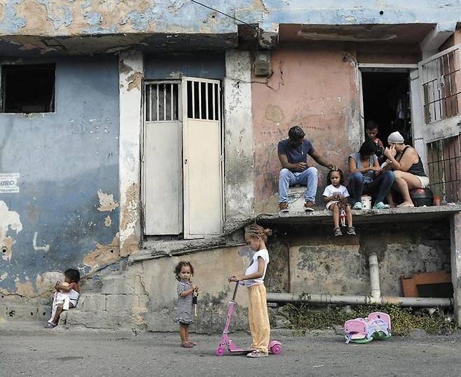 '조폭 자치 정부' 들어선 수도권 빈민가 - 지난해 12월 25일(현지 시각) 크리스마스 날 베네수엘라 수도 카라카스의 빈민 지역 페타레에서 주민과 아이들이 낡고 허름한 집에서 나와 바깥에서 시간을 보내고 있다. 페타레 등과 같은 베네수엘라의 빈민가와 외곽 지역은 범죄 조직들이 실질적인‘자치 정부’역할을 하면서 통치하고 있다. 식량과 약품 등을 나눠주고, 치안을 유지하며, 문화 행사를 열기도 한다. /AP 연합뉴스