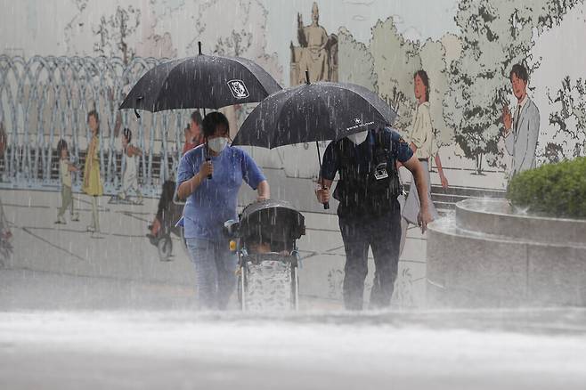 Assistant Inspector Byun Young-woo holds an umbrella for a mother and a child while escorting them to a place where they could take shelter from the rain on Wednesday. (Lee Jeong-a/The Hankyoreh)