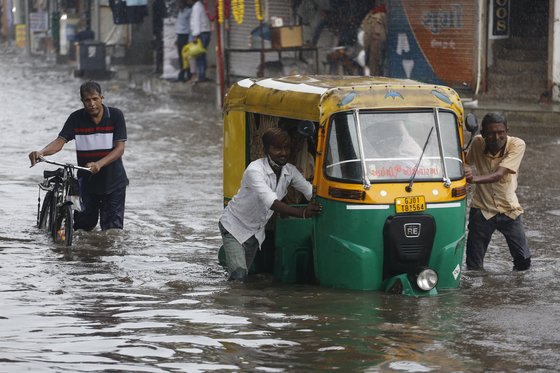 아시아 지역에 여름 몬순이 닥친 가운데 지난 22일 인도 아메다바드 주민이 폭우에 침수된 자동인력거(오토릭샤)를 밀고 있다. [AP=연합뉴스]
