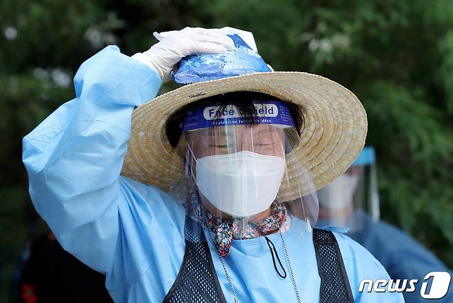 찜통더위가 이어진 21일 오후 서울 동작구보건소 앞에 설치된 선별진료소에서 얼음조끼를 입은 의료진이 머리에 아이스팩을 대고 잠시 휴식을 취하고 있다. 2021.7.21/뉴스1 © News1 박지혜 기자