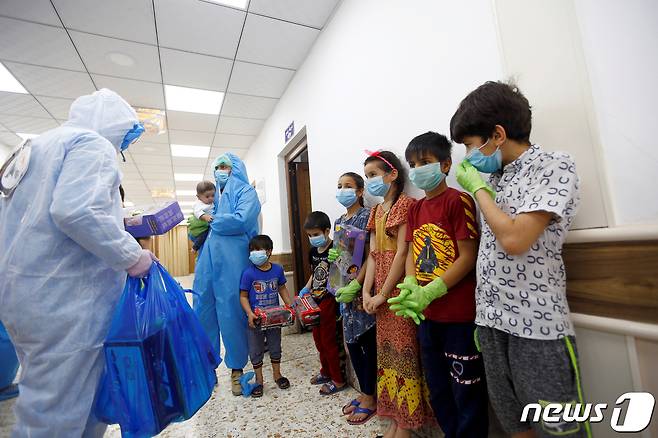 이라크 나자프의 한 코로나19 격리병동에서 2020년 4월 15일 간호사와 자원봉사자들이 방호복을 입고 아이들에게 선물을 주는 모습.  © 로이터=뉴스1